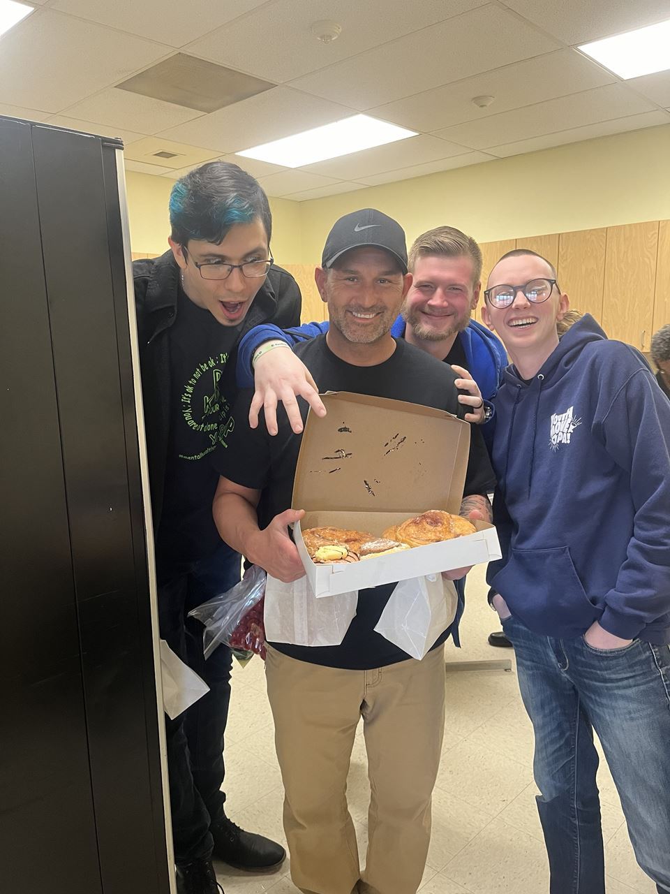 Four people smiling with a box of donuts